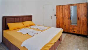 A modern bedroom featuring a yellow bedspread, towels, and a wooden wardrobe.